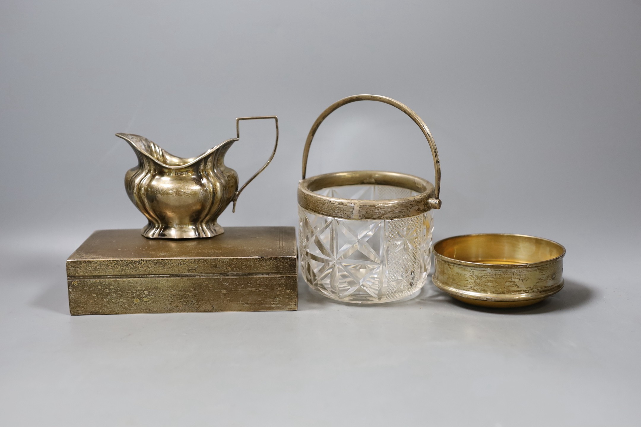A silver cigarette box, 16.7cm, a silver cream jug, a silver mounted glass jar and a modern silver mounted coaster.